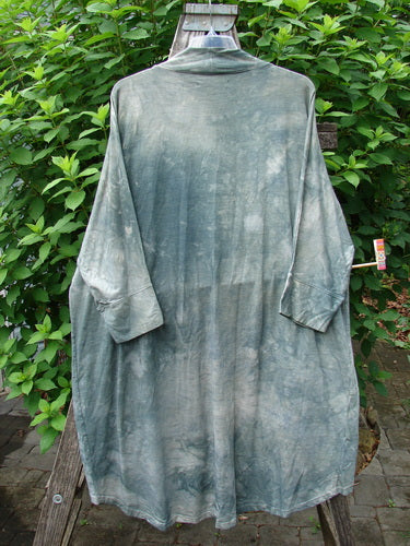 Barclay Bamboo Dolman Day Jacket Unpainted Mottled Field Grass OSFA on a clothes rack, showcasing its open front, cuffed dolman sleeves, exterior pockets, and unique rounded hemline design.