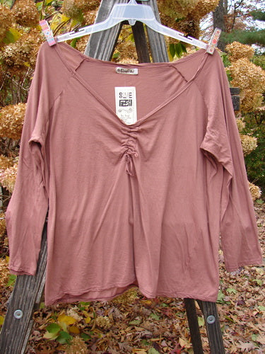 Barclay NWT Batiste Decora Ragtime Raglan Heirloom Size 2 ai: A pink shirt on a clothes rack, featuring a deep V-shaped neckline and adjustable drawcord accent.