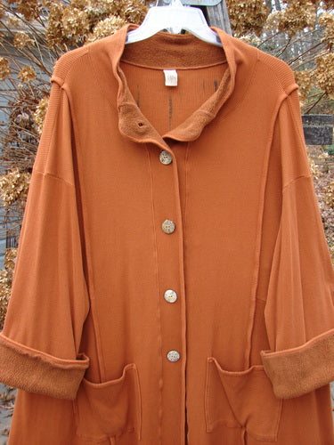Barclay Thermal Mock Collar Coat, pumpkin-colored outerwear with wooden-like textured buttons, wide longer sleeves, and a sweeping A-line shape.