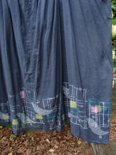 Barclay Batiste banded-collar slip dress in black, size 2, with a dark batiste body and a Birdy border of pale grid lines, small pastel squares, and curved bird motifs along the hem. The fabric hangs in soft vertical folds, with the decorative band concentrated at the lower edge.