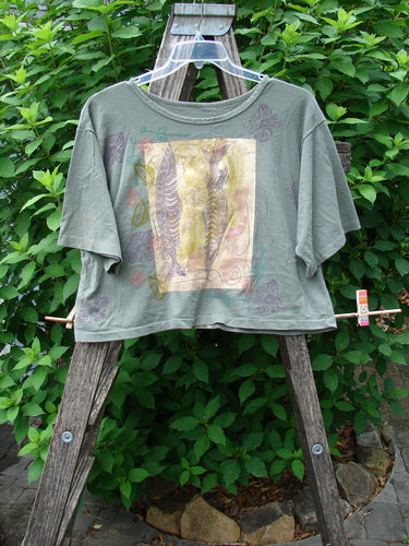 1991 Short Sleeved Crop Tee Fish Flower Olive Drab OSFA displayed on a wooden ladder, showcasing its vintage rolled neckline and unique double fish and continuous flower design.