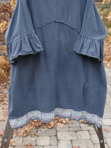 A Barclay Decora Brushed Twill Flutter Coat in Navy, featuring a blue dress with ruffles on a rack. The dress has a deep V-shaped neckline, matching buttons, and flutter ruffle 3/4 length sleeves. It also has giant round bottom pockets and a paneled, swingy hemline. Made from a heavy brushed cotton twill, this coat is perfect for a casual yet stylish look.