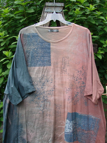 Barclay Art Tee Bicycle Floral Basket Mottled Mauve Gray OSFA displayed outdoors on a hanger, showcasing its tunic length, drop shoulders, three-quarter sleeves, rounded neckline, and varying hemline.