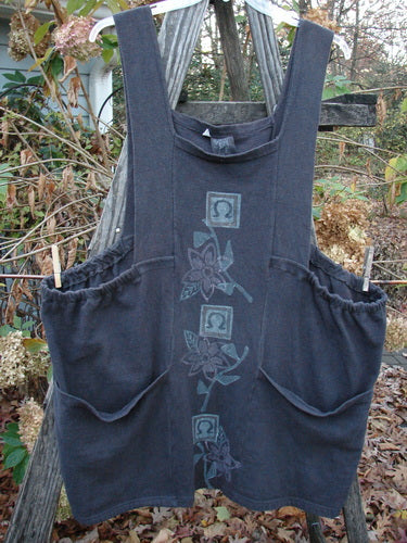 1995 Reprocessed Cottage Jumper Floral Vine Granite Size 3 hangs on a wooden pole, showcasing its thick shoulder straps, sectional bib, elastic sides, and large front pockets with a floral vine design.