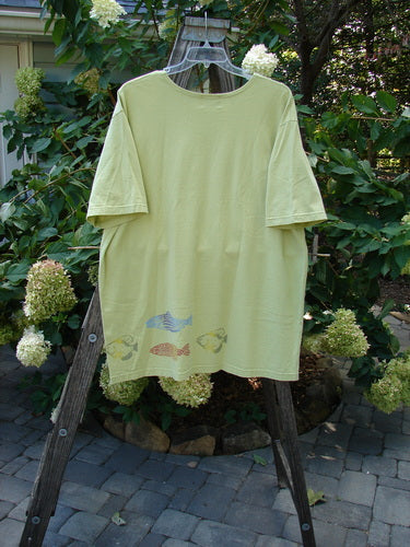 2000 Short Sleeved Tee Fish School Key Lime Pie Size 2 displayed on a wooden hanger outdoors, showcasing its drop shoulders, wide sleeves, and generous length against a natural backdrop.