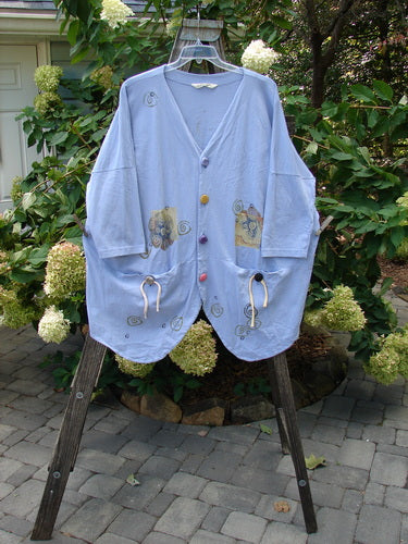 1997 Day Jacket Curl Wind Freesia OSFA on a rack, featuring assorted vintage buttons, front drop pockets, dolman sleeves, and a rounded hemline with a draw cord.