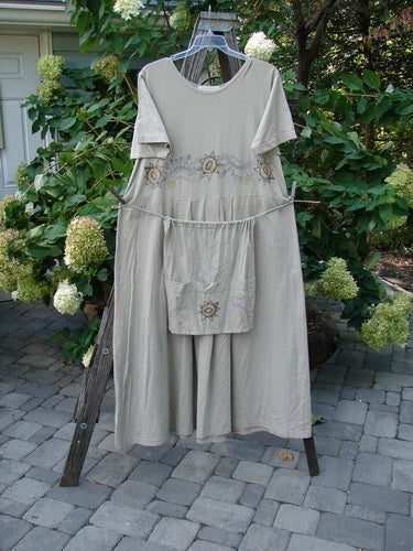 1997 Lawn Dress Star Path Wheat Size 2 displayed on a clothes rack, featuring a detachable apron with sectional pockets and tailored pleats, showcasing Blue Fish's vintage creative design.