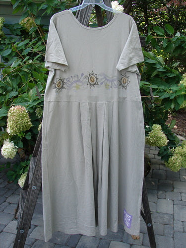 1997 Lawn Dress Star Path Wheat Size 2 features a long, organic cotton dress with tailored pleats, a detachable apron with pockets, and a unique star path design, displayed on a clothes rack.