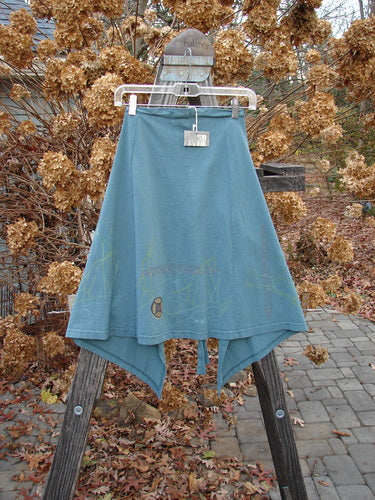 2000 NWT Grid Patch Wrap Skirt, a blue skirt on a rack. Features include a long belt, directional paint, cross-stitched accents, sectional panels, and a huge painted patch. Versatile as a mini skirt or over straight bottoms. Measurements: Long Length 27, Shorter Length 23, Width 56 inches.