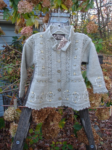 Tara Handknits NWT Kids Wild Smock Sweater Jacket Size Medium displayed on a hanger, showcasing intricate knit patterns, lace collar, large buttons, and front pockets, reflecting a handcrafted, vintage aesthetic.