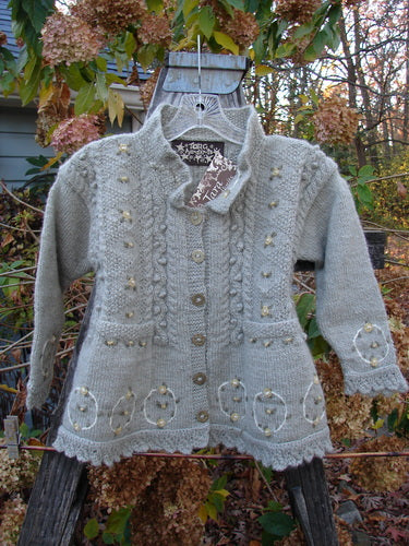 Tara Handknits NWT Kids Wild Smock Sweater Jacket Size Medium displayed on a swinger, showcasing its intricate knit patterns, lace collar, oversized gold buttons, and two front pockets.