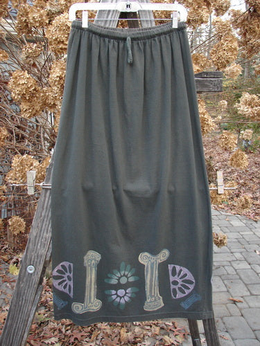 1993 Drawcord Skirt Column Black Sand Size 2: A long grey skirt with a painted design on it, featuring a full elastic and rope waistline. The skirt has a slight bottom flare and measures 36 inches in length.