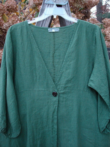 A green linen cardigan with deep V neckline and single button closure, empire waist seam, billowy sleeves, and A-line shape.