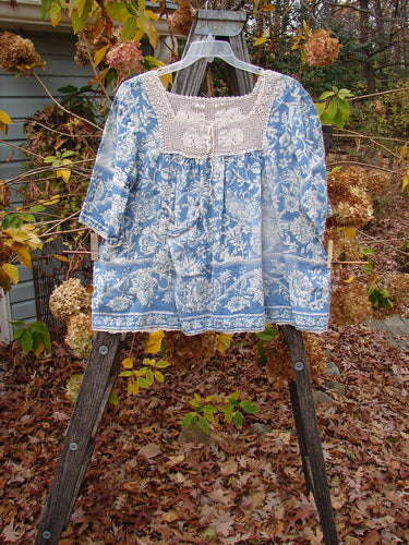 Magnolia Pearl Homespun Linen Crochet Bunny Blouse Tapestry Blue displayed on a wooden stand, featuring a crochet square neckline, three-quarter sleeves, and a front drop pocket.