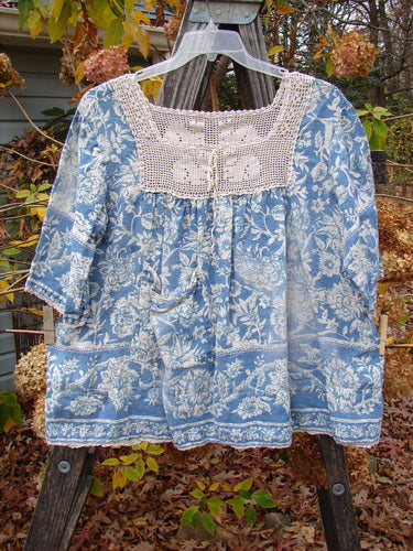 Magnolia Pearl Homespun Linen Crochet Bunny Blouse Tapestry Blue OSFA displayed on a hanger, featuring a crochet square neckline, three-quarter sleeves, and a front drop pocket.