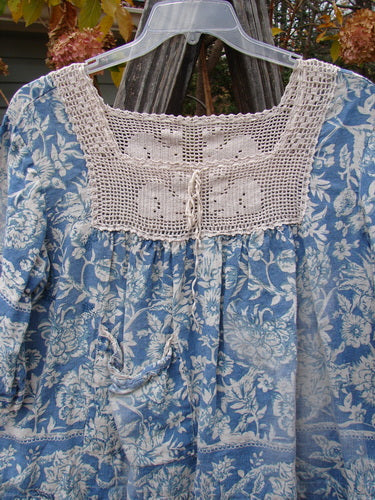 Magnolia Pearl Homespun Linen Crochet Bunny Blouse in Tapestry Blue, featuring a floral pattern, crochet square neckline, three-quarter billowing sleeves, and front pocket on a hanger.