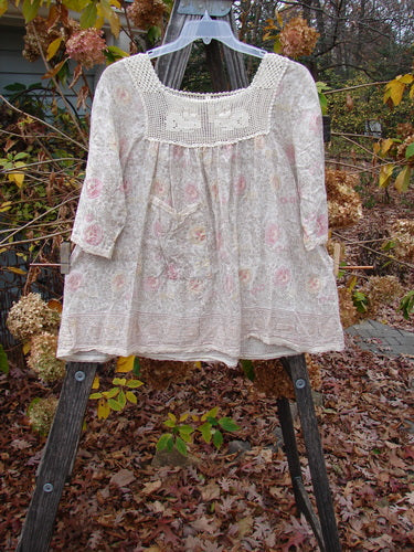 Magnolia Pearl Batiste Cotton Crochet Bunny Blouse Field Florals OSFA displayed on a wooden stand, showcasing its crochet neckline, billowing sleeves, and front drop pocket, embodying vintage-inspired design.