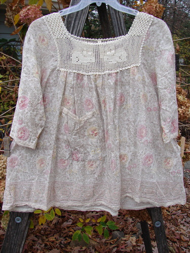 Magnolia Pearl Batiste Cotton Crochet Bunny Blouse Field Florals OSFA features a white dress with pink floral patterns, crochet square neckline, three-quarter sleeves, and a front side drop pocket.