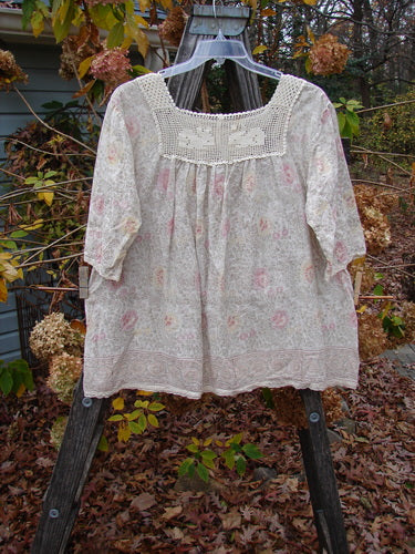 Magnolia Pearl Batiste Cotton Crochet Bunny Blouse Field Florals OSFA displayed on a hanger, showcasing its crochet square neckline, floral pattern, three-quarter sleeves, and front pocket detail.