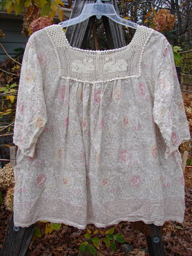 Magnolia Pearl Batiste Cotton Crochet Bunny Blouse Field Florals OSFA displayed on a clothes rack, featuring a crochet square neckline, three-quarter sleeves, and a wide lower flair with a front pocket.