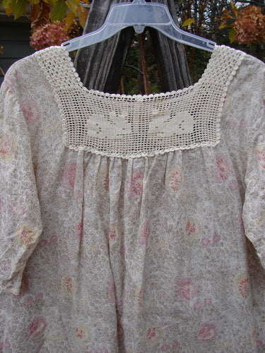 Magnolia Pearl Batiste Cotton Crochet Bunny Blouse Field Florals OSFA, featuring a lace design with crochet neckline, floral pattern, and three-quarter sleeves, displayed on a hanger.