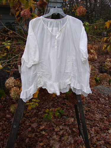 Magnolia Pearl Silk Voile Gather Drapery Top White OSFA displayed on a rack, showcasing its ruffled hem, Henley button line, and three-quarter sleeves, embodying the creative vintage style of Bluefishfinder.com.