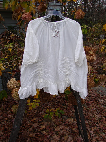 Magnolia Pearl Silk Voile Gather Drapery Top White OSFA displayed outdoors on a hanger, showcasing its full ruffled hem, three-quarter sleeves, and vertical gathers, embodying vintage style and individuality.