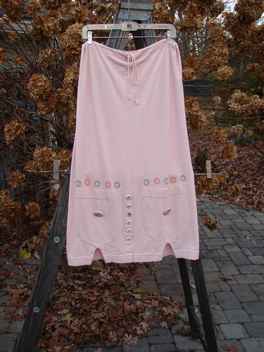 2001 Wishpocket Skirt Button Path Pink Tile Size 1: A light pink skirt with buttons and a drawstring waist. Features oversized pockets and ceramic accent buttons. Made from organic cotton.