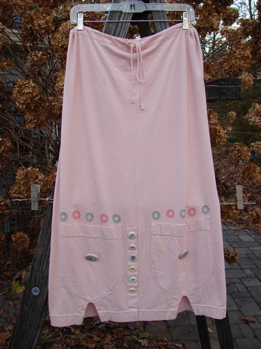 2001 Wishpocket Skirt Button Path Pink Tile Size 1: A pink skirt with buttons and pockets on a clothesline. Organic cotton, drawstring waist, ceramic accents.