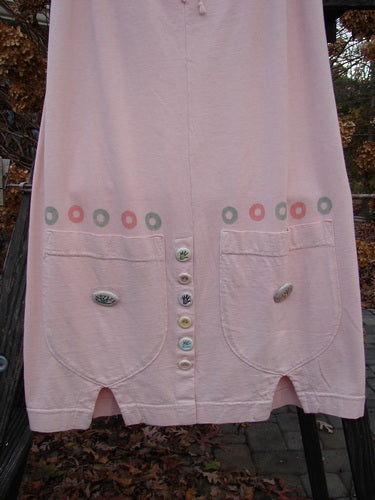 2001 Wishpocket Skirt Button Path Pink Tile Size 1: A pink dress with buttons, featuring a 1/2 front drawstring waist, oversized rounded pockets, and ceramic accent buttons.