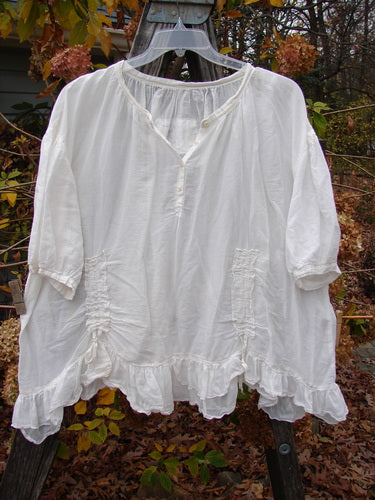 Magnolia Pearl Silk Voile Gather Drapery Top White OSFA displayed on a hanger, showcasing its full ruffled hem, Henley button line, and three-quarter sleeves with a widening lower flair.