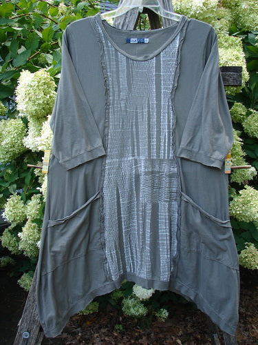 Barclay Raw Edge Flutter Drop Pocket Tunic Woods in darkest sand, size 0, with a soft draped silhouette, raw edges, flutter sleeves, and oversized drop pockets. The textured gray-green fabric is layered over a patterned center panel, creating a loose, asymmetrical fall.