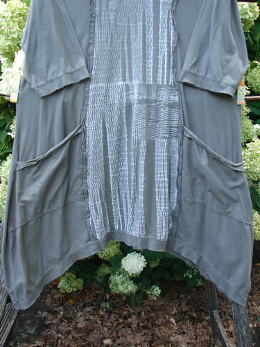 Barclay Raw Edge Flutter Drop Pocket Tunic in darkest sand, size 0, with a loose draped silhouette, raw-edge hems, flutter sleeves, and oversized drop pockets. The soft, matte fabric is shown in layered gray-brown tones with a pale patterned center panel.