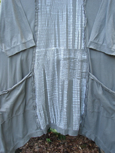 Barclay Raw Edge Flutter Drop Pocket Tunic in darkest sand, size 0, with a loose draped silhouette, raw-edged seams, flutter sleeves, and curved drop pockets. The soft, matte fabric is layered over a lighter textured center panel, creating a muted gray-brown palette.