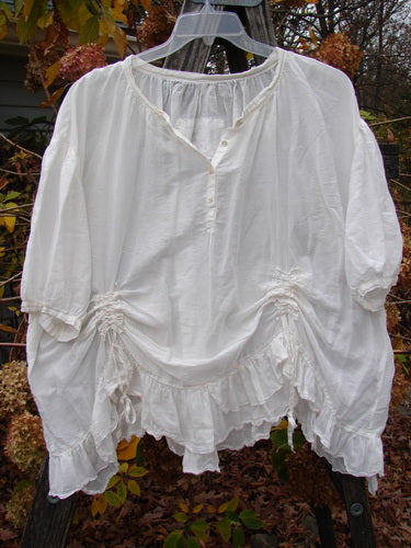 Magnolia Pearl Silk Voile Gather Drapery Top White OSFA displayed on a clothes rack, showcasing its full ruffled hem, Henley button line, and vertical gathers, embodying Bluefishfinder.com's vintage, creative style.