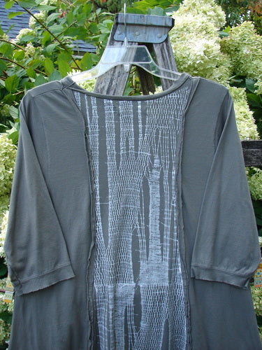Barclay Raw Edge Flutter Drop Pocket Tunic in darkest sand, size 0, with a soft draped silhouette, raw-edged seams, and flutter sleeves. The front panel shows a vertical abstract print in pale gray against muted charcoal, hanging on a clear hanger outdoors.