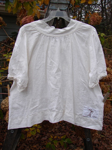 Magnolia Pearl Homespun Linen Lace Button Bib Top Farm Love Off White OSFA hanging on a clothesline, showcasing three-quarter length sleeves, lace accents, and a unique hemline design.