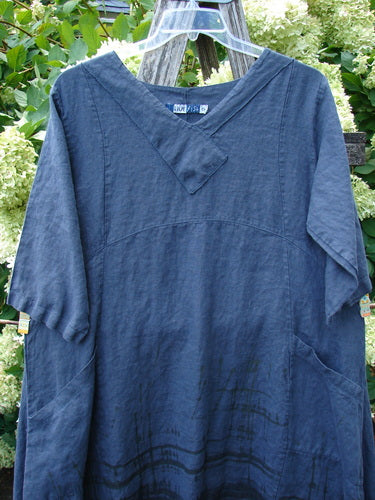 Barclay Linen Cross Over Incense Dress Structural Cliff in deep navy, size 0, with a soft linen texture, crossover V-neck, and loose short sleeves. The dress hangs on a clear hanger, its relaxed shape and subtle seams set against leafy outdoor greenery.