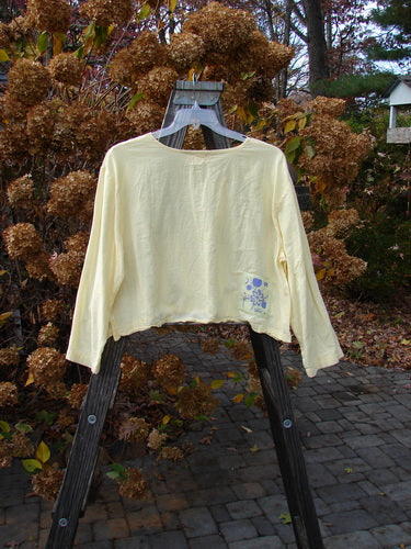1999 PMU Batiste Boxy Top Unpainted Buttercup Size 2: A yellow shirt on a wooden rack, with long billowy sleeves and a wider boxy shape.