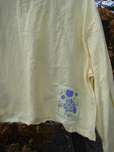 1999 PMU Batiste Boxy Top Unpainted Buttercup Size 2: A white shirt with a blue flower design, featuring a rounded neckline, billowy sleeves, and side vents. Made from breathable cotton batiste.