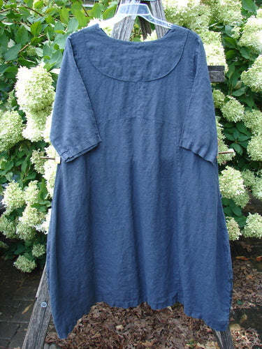 Barclay Linen Cross Over Incense Dress Structural Cliff in deep navy, size 0, with a relaxed A-line shape, rounded neckline, and short sleeves. The textured linen drapes softly from a hanger, set against leafy white hydrangeas and dark wood for a natural outdoor display.