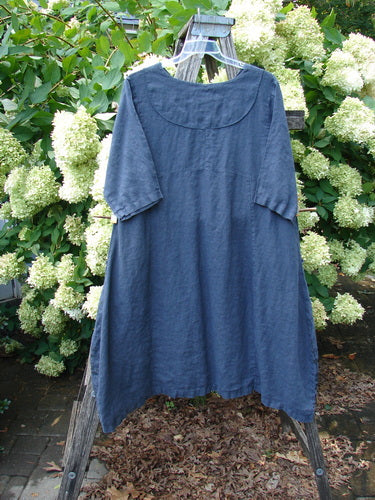 Barclay Linen Cross Over Incense Dress Structural Cliff in deep navy, size 0, hangs from a wooden A-frame amid lush white hydrangeas. The linen fabric has a softly wrinkled texture, short sleeves, and a rounded crossover neckline with a loose, structured drape.