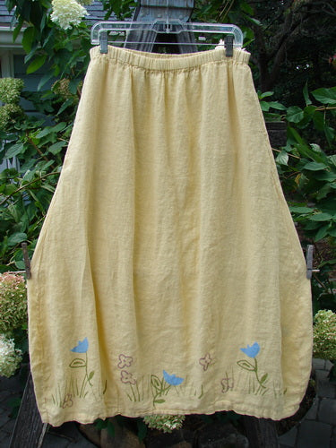 1999 Windy Day Skirt Tulip Buttercup Size 2: A yellow skirt with blue tulip patterns, featuring a full elastic waistline, reverse bell shape, and two vertical pleats, crafted from lightweight handkerchief linen.