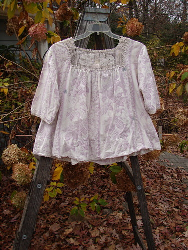 Magnolia Pearl Homespun Linen Crochet Bunny Blouse Swirl Lavender OSFA displayed outdoors on a wooden hanger, showcasing the crochet neckline, three-quarter sleeves, lace-edged details, and signature Magnolia Pearl tag.