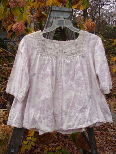 Magnolia Pearl Homespun Linen Crochet Bunny Blouse Swirl Lavender OSFA displayed on a swing, showcasing its crochet squared neckline, three-quarter sleeves, and lace-edged hem, exemplifying Bluefishfinder.com's vintage-inspired fashion offerings.