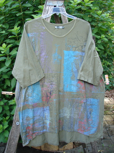 Barclay Tournesol Tunic Contour Forest Mottled Green Olive OSFA, featuring loose three-quarter sleeves, a rounded neckline, and a varying hemline, displayed on a wooden rack.