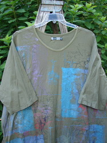 Barclay Tournesol Tunic Contour Forest Mottled Green Olive OSFA displayed on a swing, showcasing its long tunic length, drop shoulders, loose three-quarter sleeves, and varied hemline, embodying BlueFishFinder's vintage style.