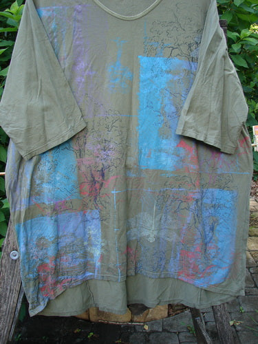 Barclay Tournesol Tunic Contour Forest Mottled Green Olive OSFA, featuring a drop shoulder, loose three-quarter sleeves, and a rounded neckline with a varying hemline, showcasing artistic blue and pink designs.