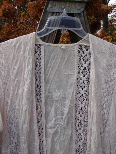 Magnolia Pearl European Cotton Embroidered Lace Duster, antique white, OSFA. Open flowing front, cap drop sleeves, gathered lace seams, matching lace hem, embroidered floral vine backdrop. Bust 66, waist 66, hips 66, sweep 70, front back length 46, sides 50 inches.