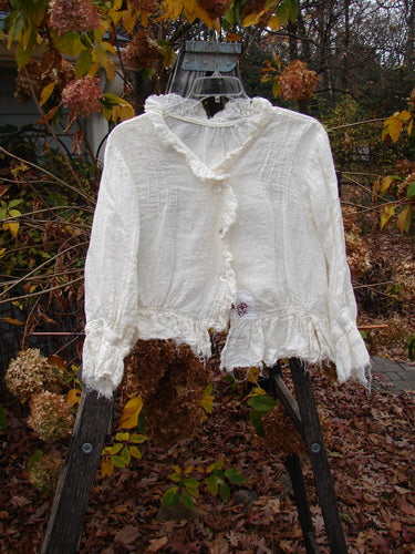 Magnolia Pearl Homespun Linen Raglan Tab Jacket Farm Love Off White OSFA displayed outdoors, showcasing its frayed sleeves, pearl button front, and distinctive embroidered details against a natural autumn backdrop.